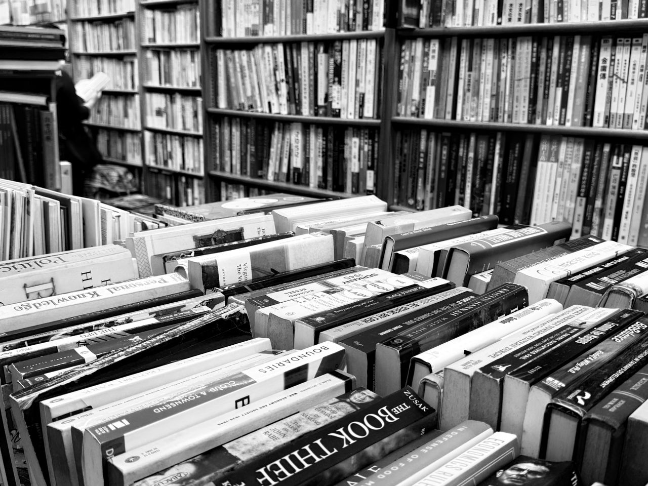 Monochrome image of a packed bookstore with multiple rows of books on shelves and tables.